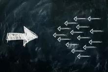 Links ein großer weißer Kreidpfeil, der nach rechts zeigt. Rechts viele weiße kleine Kreidepfeile, die nach links zeigen. Hintergrund ist eine schwarze Tafel.