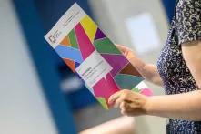 Person, dessen Oberkörper zu sehen ist, hält gedrucktes, buntes der Netzwerktagung "Antifeminismus begegnen – Demokratie stärken" 2023.