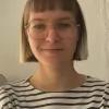 Porträtfoto von Lena Trilsbeeck: Helle Hautfarbe, kinnkurzes blondes Haar mit gradem Pony, heller Brille und schwarz-weiß-gestreiftes Shirt..